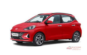 Front and side view of the 2025 Hyundai Grand i10 in red color, parked on an urban road showing its sleek design, alloy wheels, LED DRLs, and modern styling features.