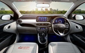 Front and side view of the 2025 Hyundai Grand i10 in red color, parked on an urban road showing its sleek design, alloy wheels, LED DRLs, and modern styling features.